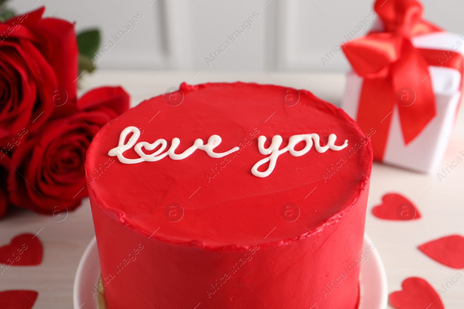 Photo of Bento cake with text Love You, roses, paper hearts and gift box on white table, closeup. St. Valentine's day surprise