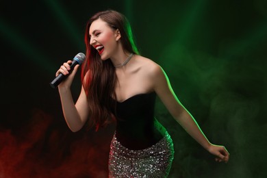 Emotional woman with microphone singing on stage in color lighted smoke