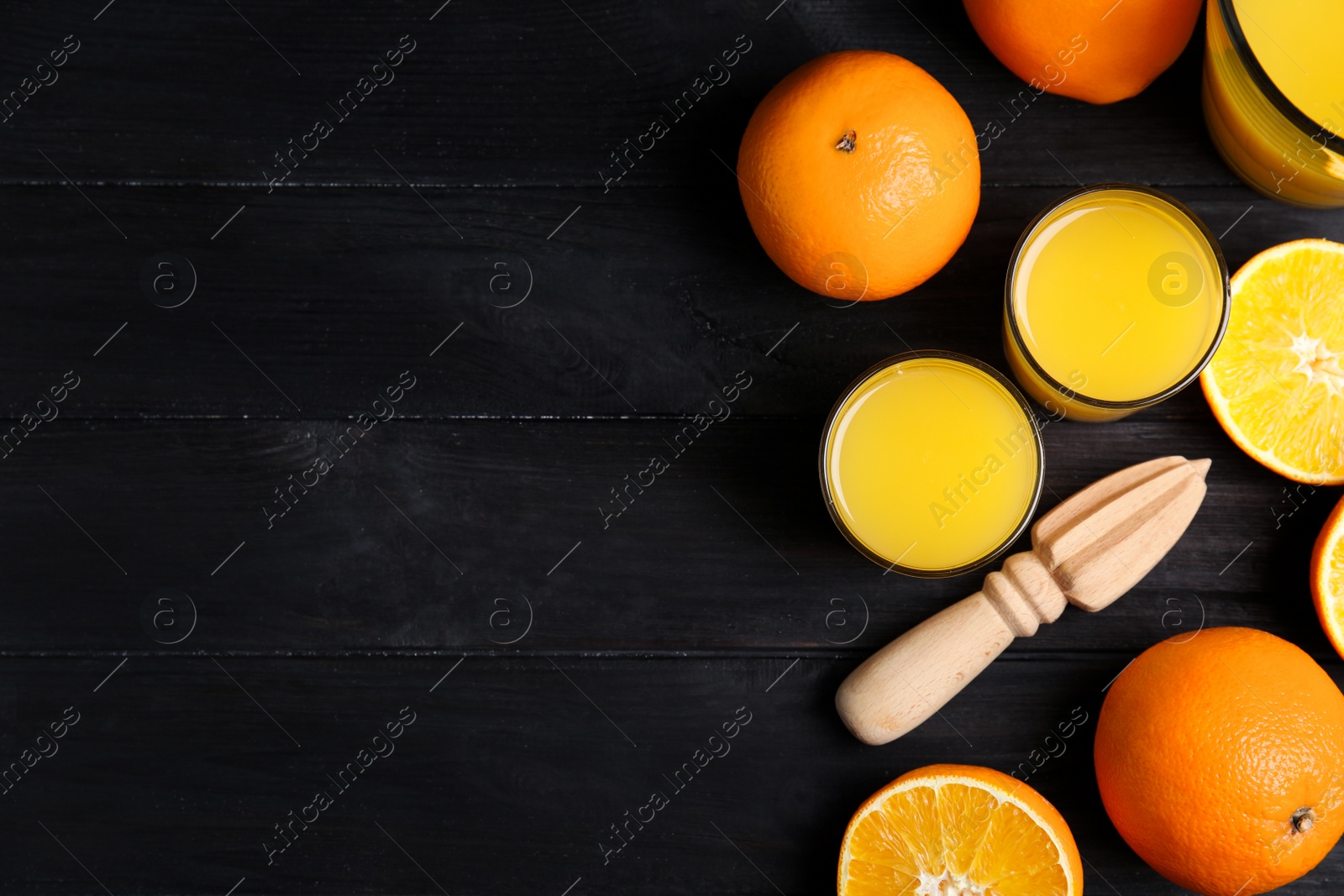 Photo of Fresh ripe oranges, juice and reamer on dark wooden table, flat lay. Space for text