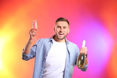 Portrait of happy man holding bottle and glass with champagne on color background