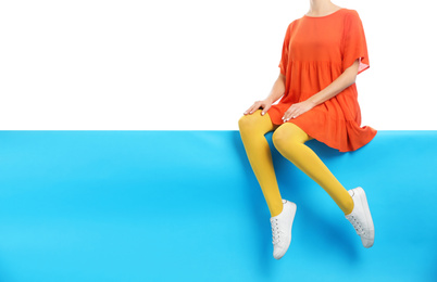 Woman wearing yellow tights and stylish shoes sitting on color background, closeup. Space for text