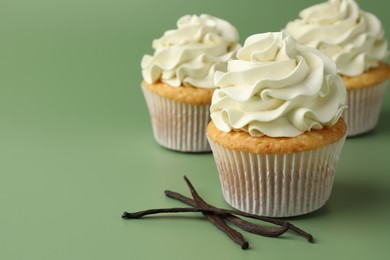 Photo of Tasty cupcakes with cream and vanilla pods on green background, closeup. Space for text