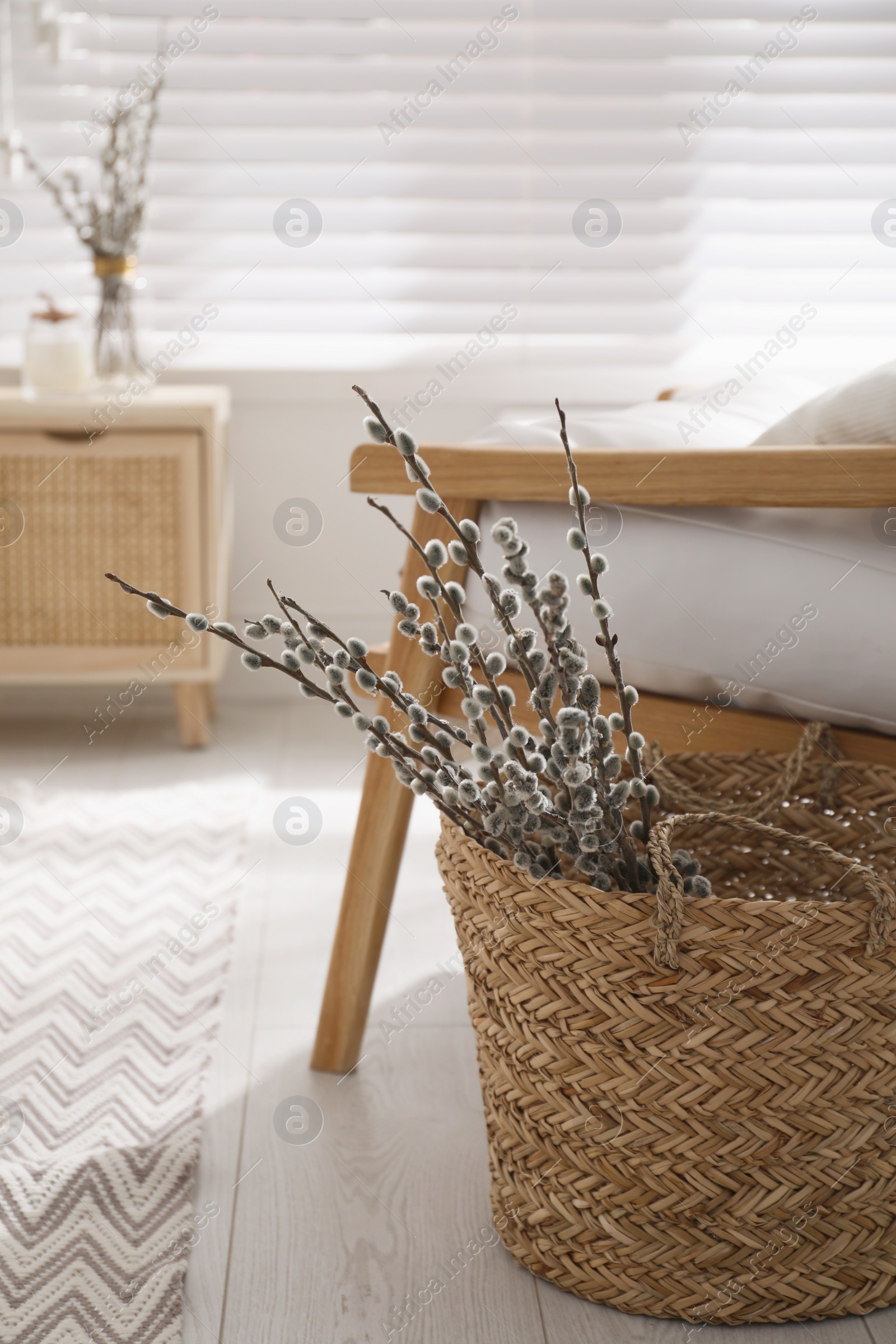 Photo of Wicker basket with pussy willow tree branches near armchair in room