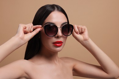 Photo of Attractive woman wearing fashionable sunglasses against beige background