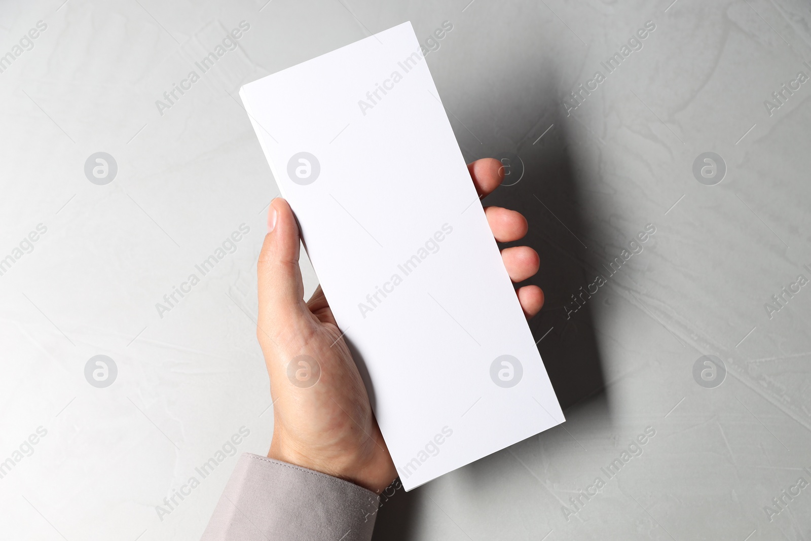 Photo of Man holding white blank card at light grey table, top view. Mockup for design