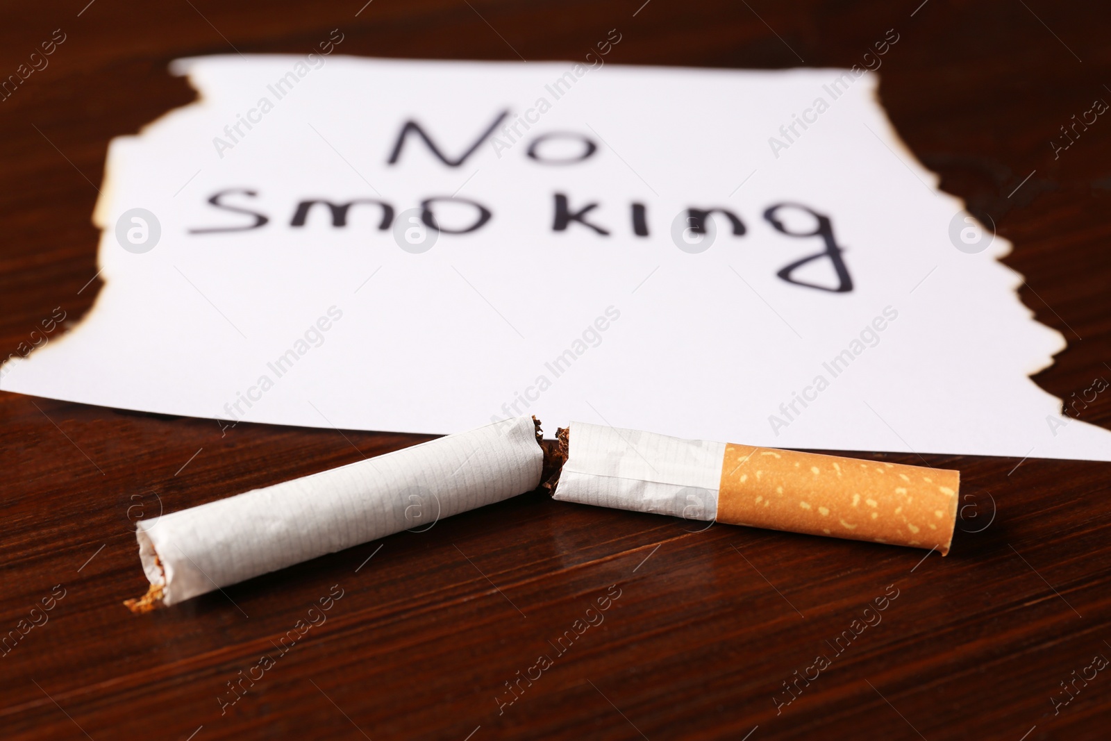 Photo of Broken cigarette and words No Smoking written on paper on wooden table, closeup