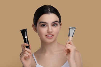 Photo of Teenage girl holding tubes with foundation on beige background