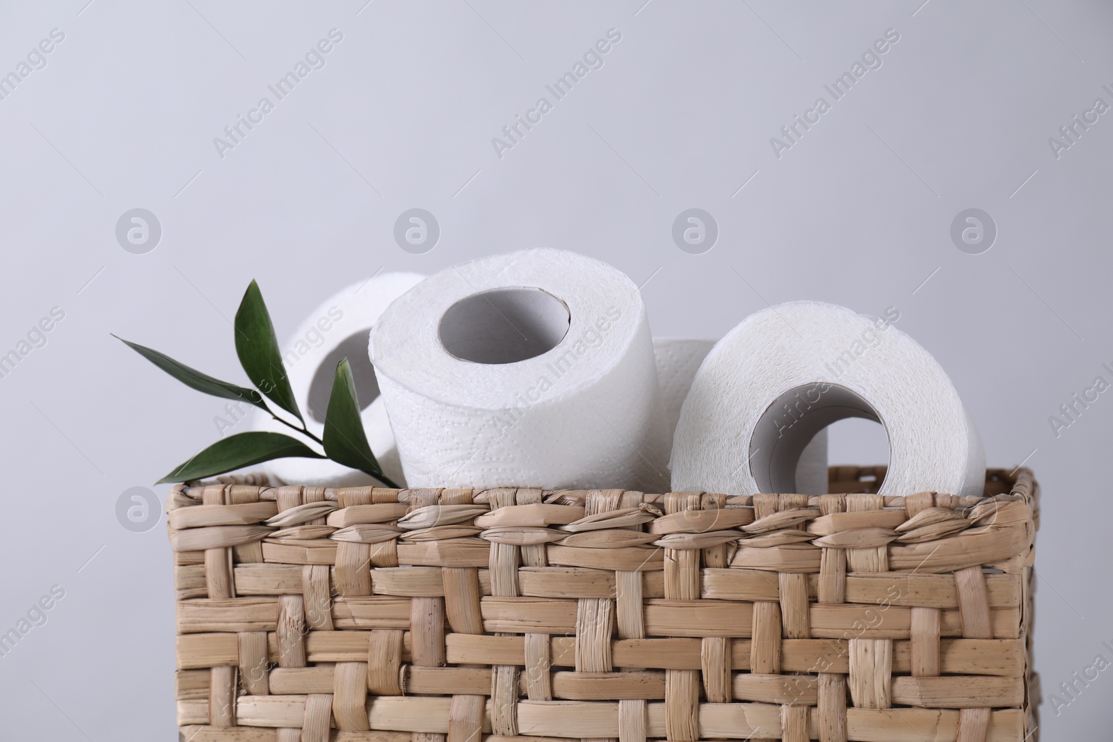 Photo of Toilet paper rolls and green leaves in wicker basket against light grey wall