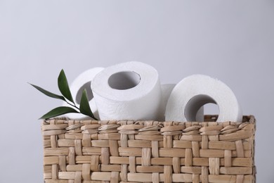 Toilet paper rolls and green leaves in wicker basket against light grey wall