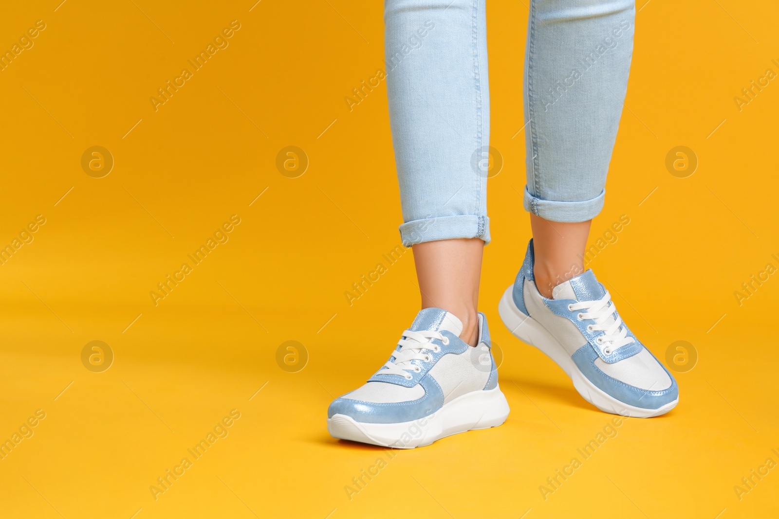 Photo of Woman wearing stylish sneakers on yellow background, closeup. Space for text