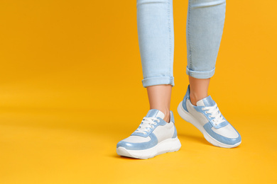 Woman wearing stylish sneakers on yellow background, closeup. Space for text