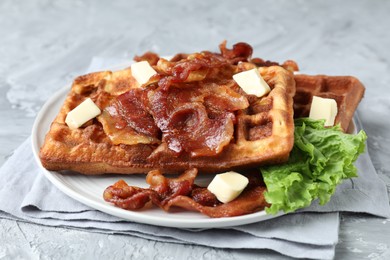Photo of Delicious Belgium waffles served with fried bacon and butter on grey table, closeup