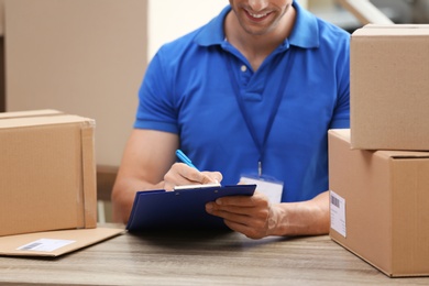 Young courier working with papers among parcels at table in delivery department