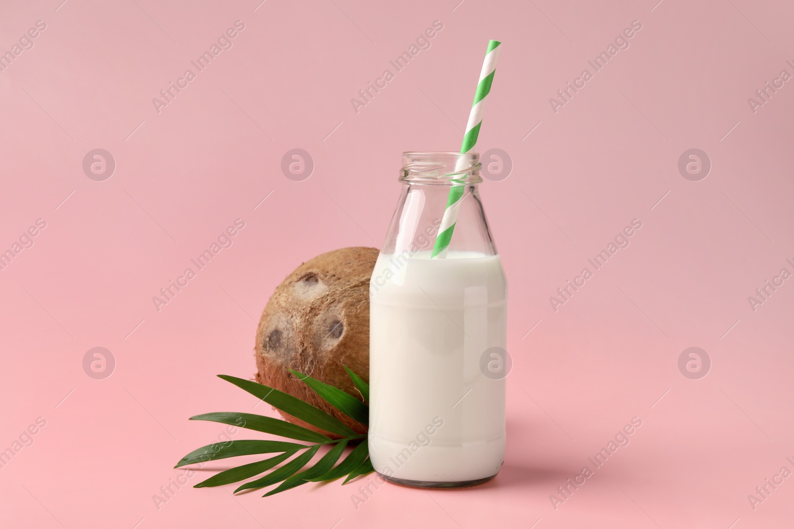 Photo of Glass bottle of delicious vegan milk, coconut and leaf on pink background