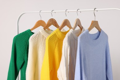 Photo of Rack with different warm sweaters on light background