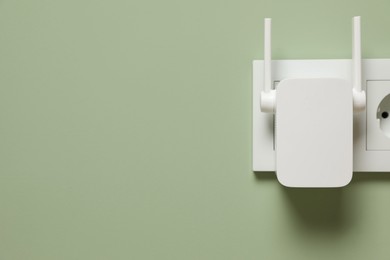 Photo of Wireless Wi-Fi repeater on light green wall, space for text