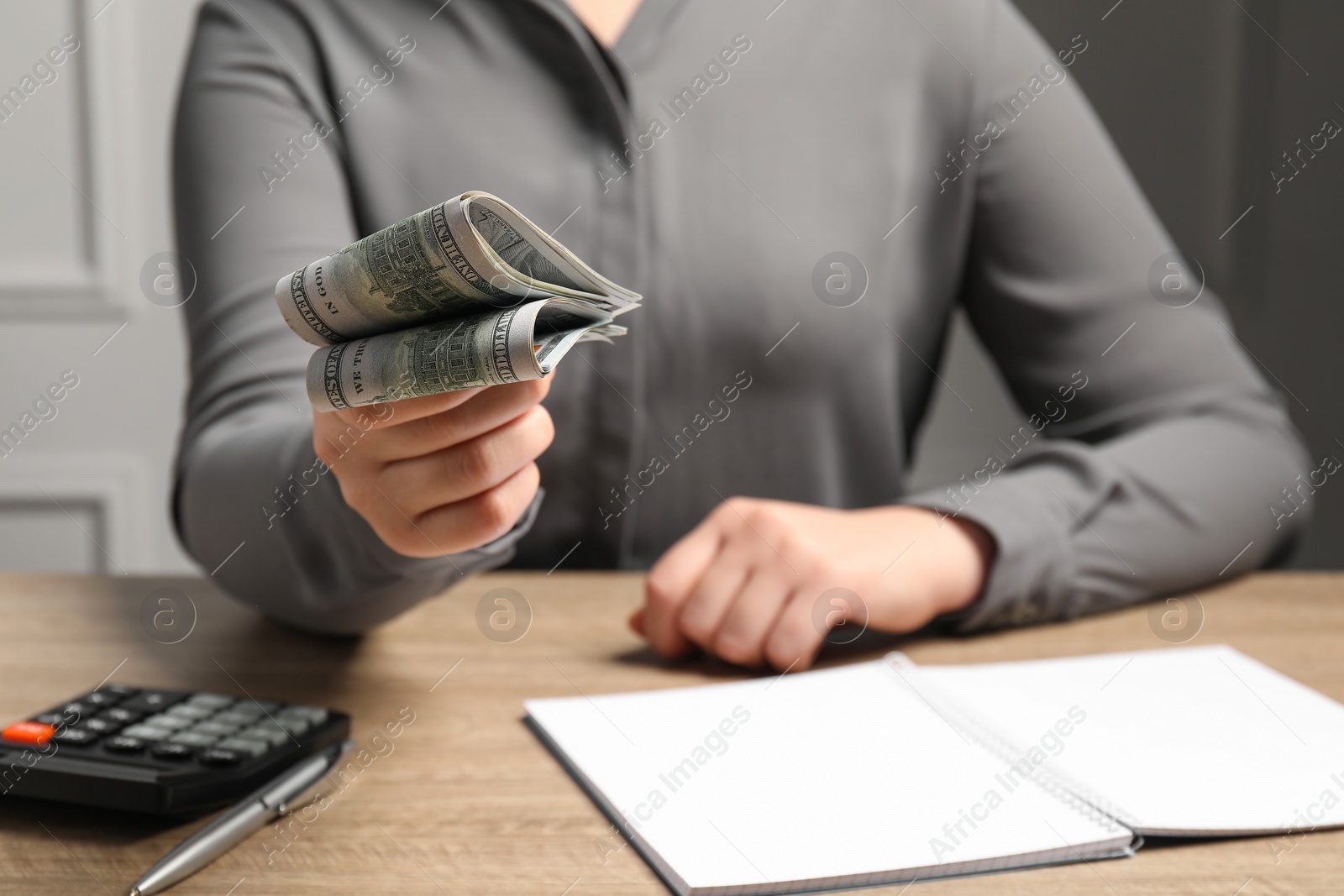 Photo of Money exchange. Woman holding dollar banknotes at wooden table, closeup