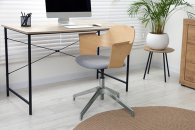 Photo of Stylish office interior with comfortable chair, desk and houseplant