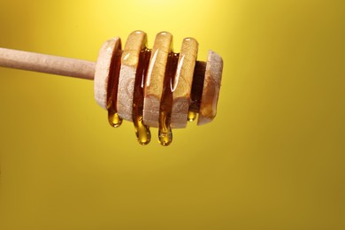 Photo of Delicious honey flowing down from dipper against golden background, closeup. Space for text