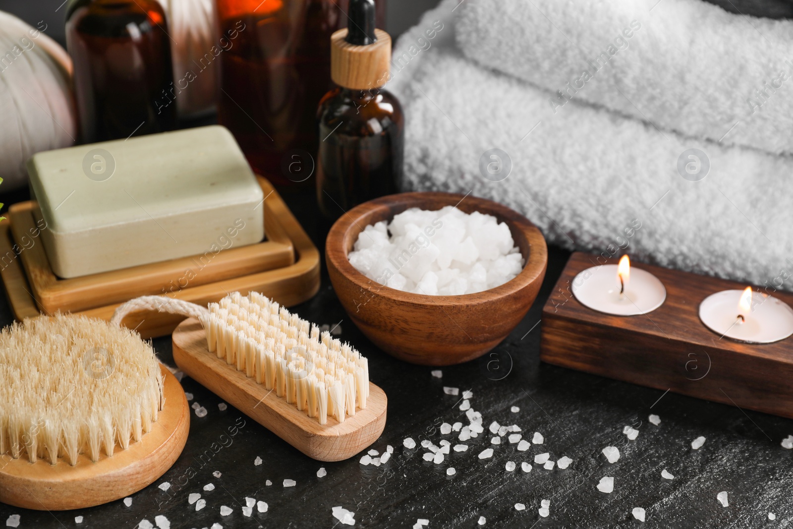 Photo of Spa composition. Brushes, soap bar, sea salt and burning candles on black table