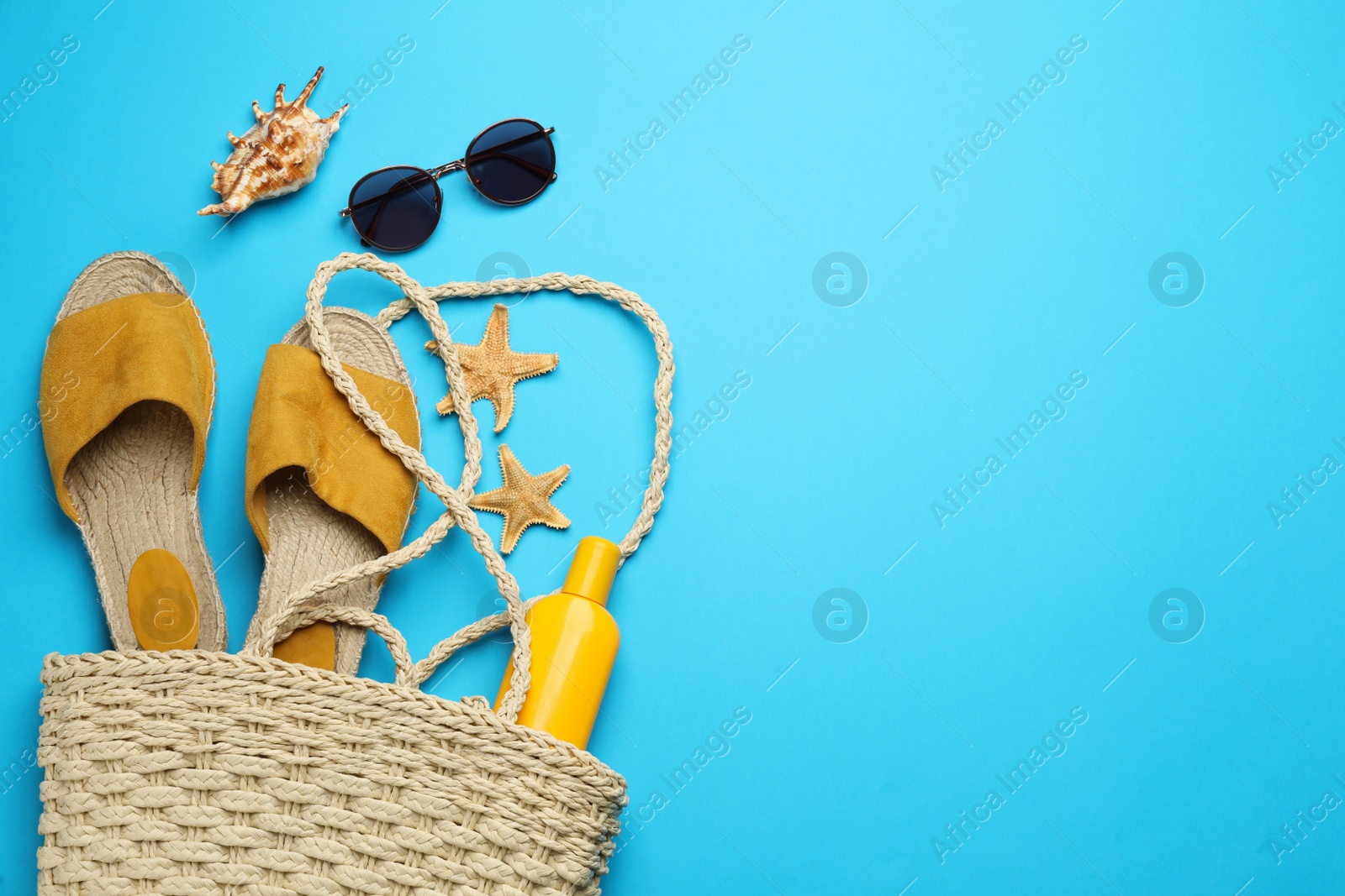 Photo of Stylish bag with beach accessories on light blue background, flat lay. Space for text