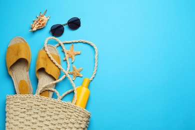 Photo of Stylish bag with beach accessories on light blue background, flat lay. Space for text