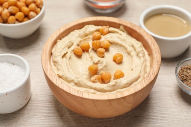 Photo of Bowl with delicious hummus and chickpeas on light wooden table, closeup