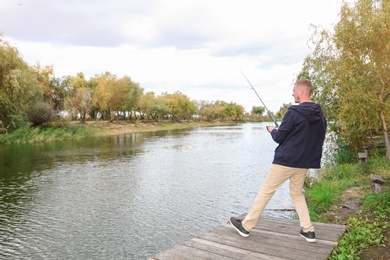 Man fishing on wooden pier at riverside. Recreational activity