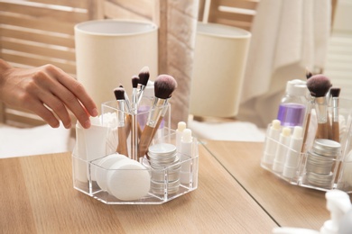 Woman taking tube with cream from organizer for cosmetic products on table