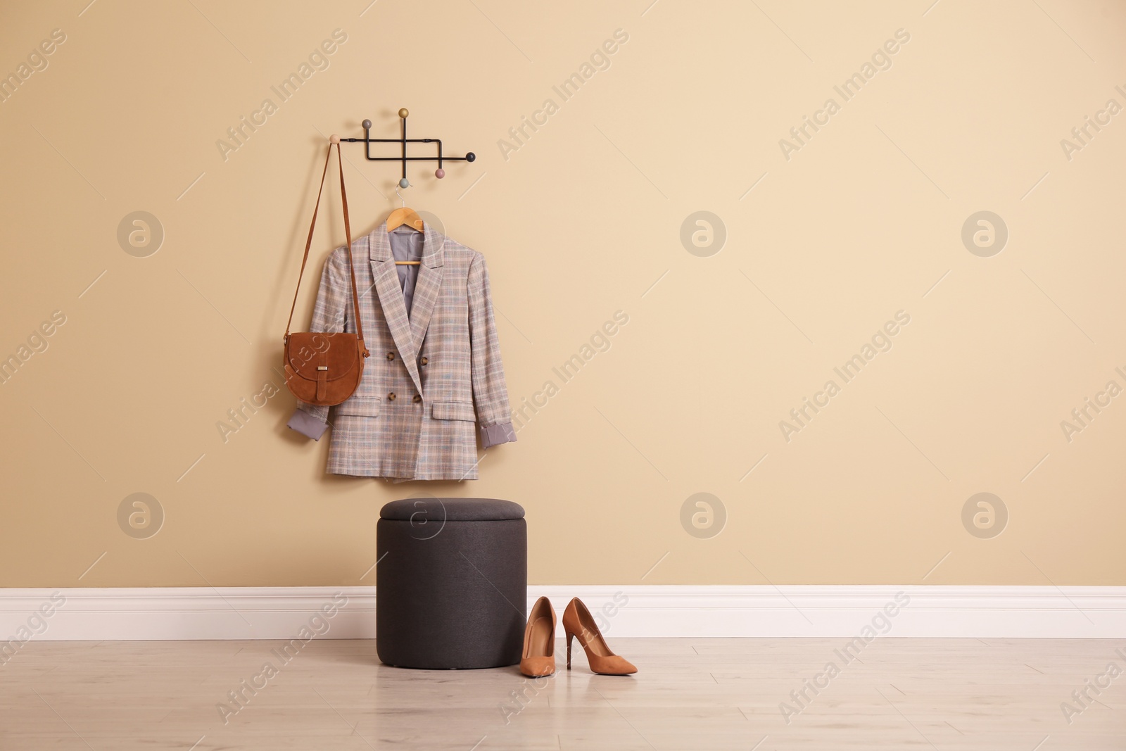 Photo of Stylish comfortable pouf near beige wall in hallway, space for text