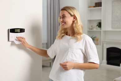 Photo of Smiling woman entering code on home security system in room