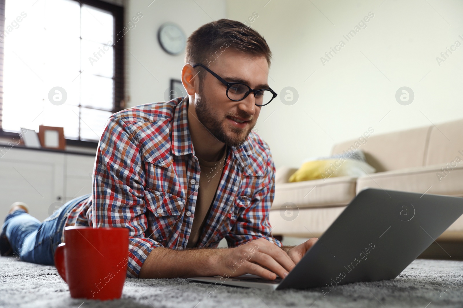 Photo of Young man using laptop while lying on floor in living room