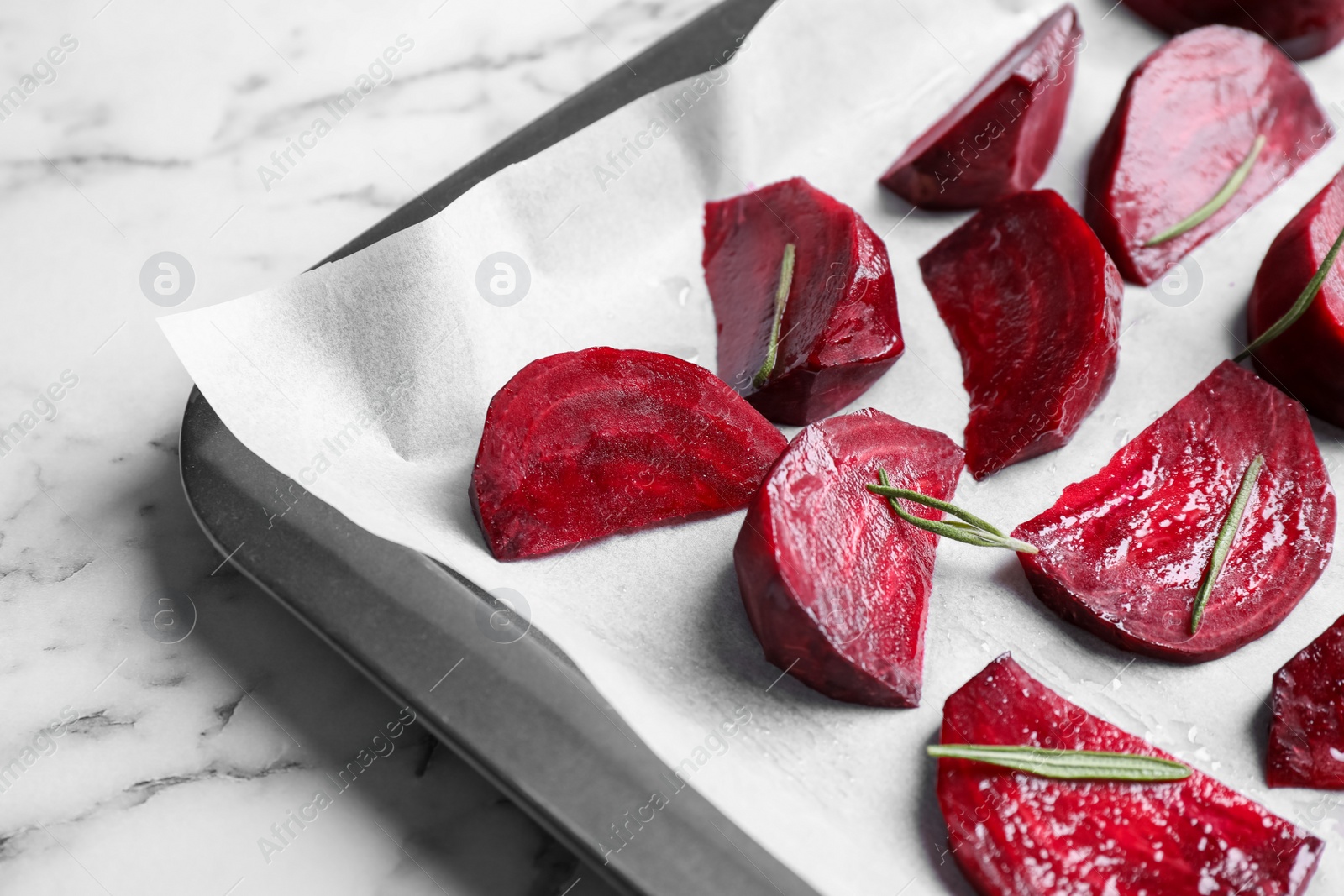 Photo of Baking tray with raw beetroot slices and rosemary on white marble table, closeup