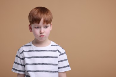 Portrait of sad little boy on beige background, space for text