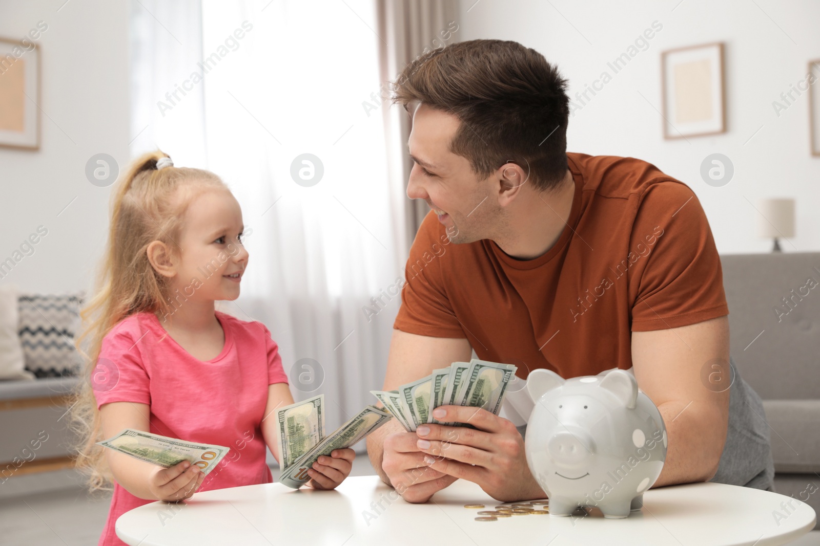 Photo of Father and daughter counting money at table indoors