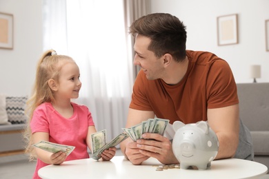 Father and daughter counting money at table indoors