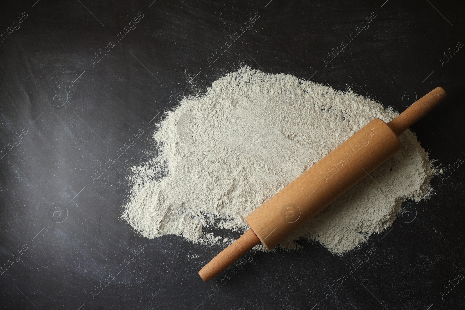 Photo of Flour and rolling pin on black table, top view