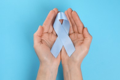 International Psoriasis Day. Woman with light blue ribbon as symbol of support on light blue background, top view