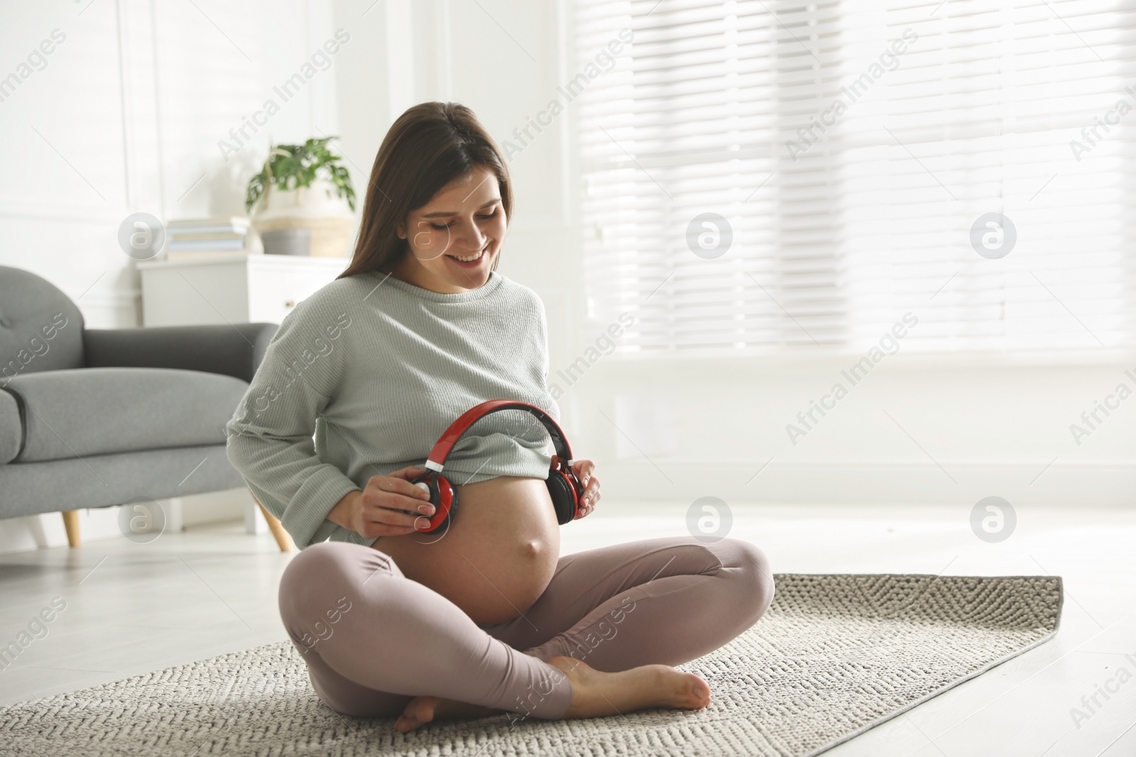 Photo of Beautiful pregnant woman with headphones on her belly at home