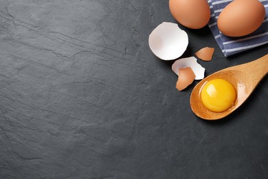 Photo of Raw chicken eggs and spoon with yolk on black table, flat lay. Space for text