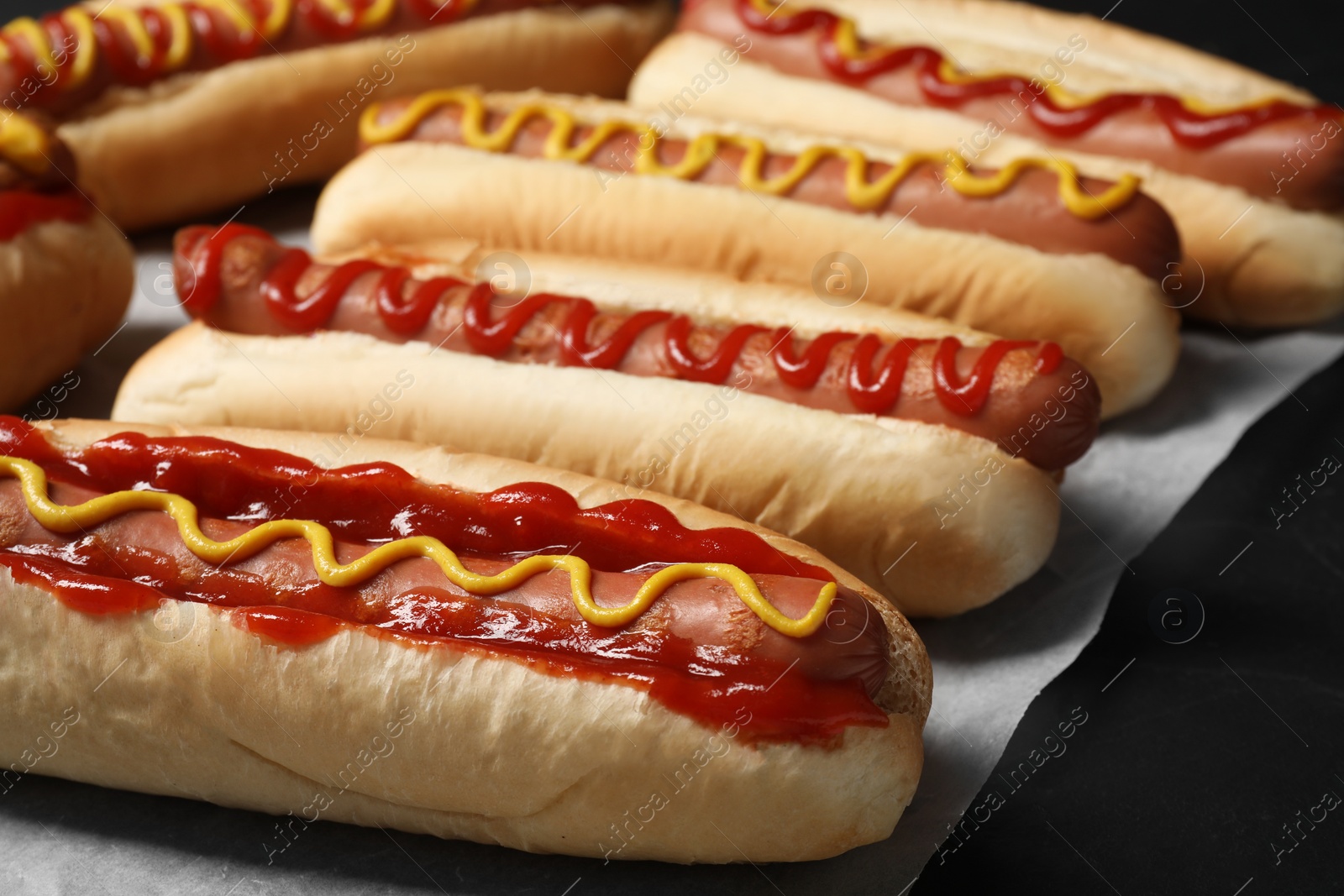 Photo of Fresh delicious hot dogs with sauces on black table, closeup