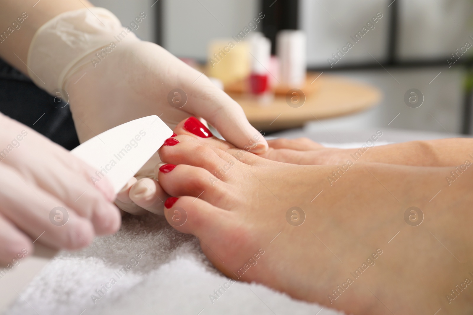 Photo of Pedicurist filing client`s toenails in beauty salon, closeup