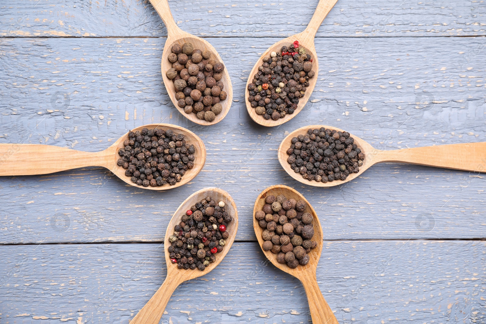 Photo of Spoons with peppercorns on grey wooden table, flat lay