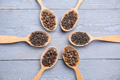 Spoons with peppercorns on grey wooden table, flat lay