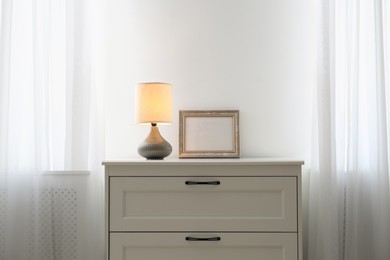 Photo of Modern chest of drawers with lamp near window in room