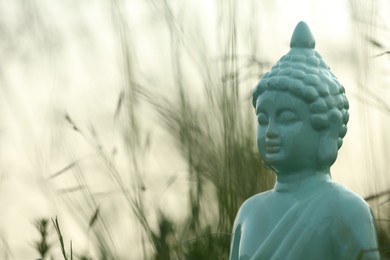 Photo of Decorative Buddha statue in green grass outdoors, closeup. Space for text