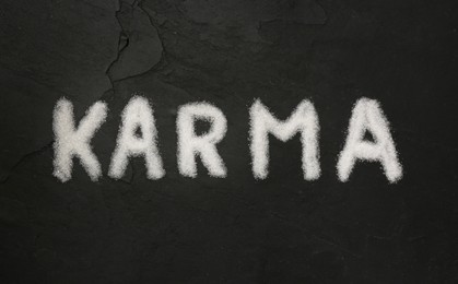 Photo of Word Karma made of sea salt on dark background, flat lay