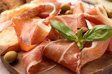 Photo of Slices of tasty cured ham, olives, bread and basil on wooden board, closeup