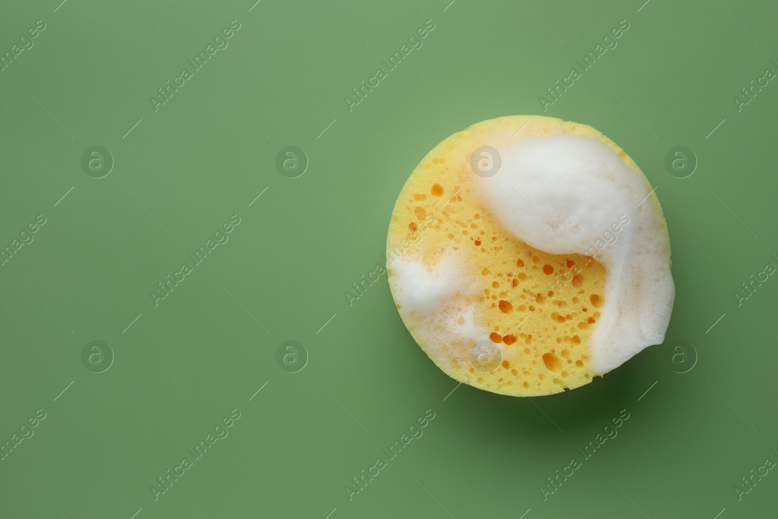 Photo of Yellow sponge with foam on green background, top view. Space for text