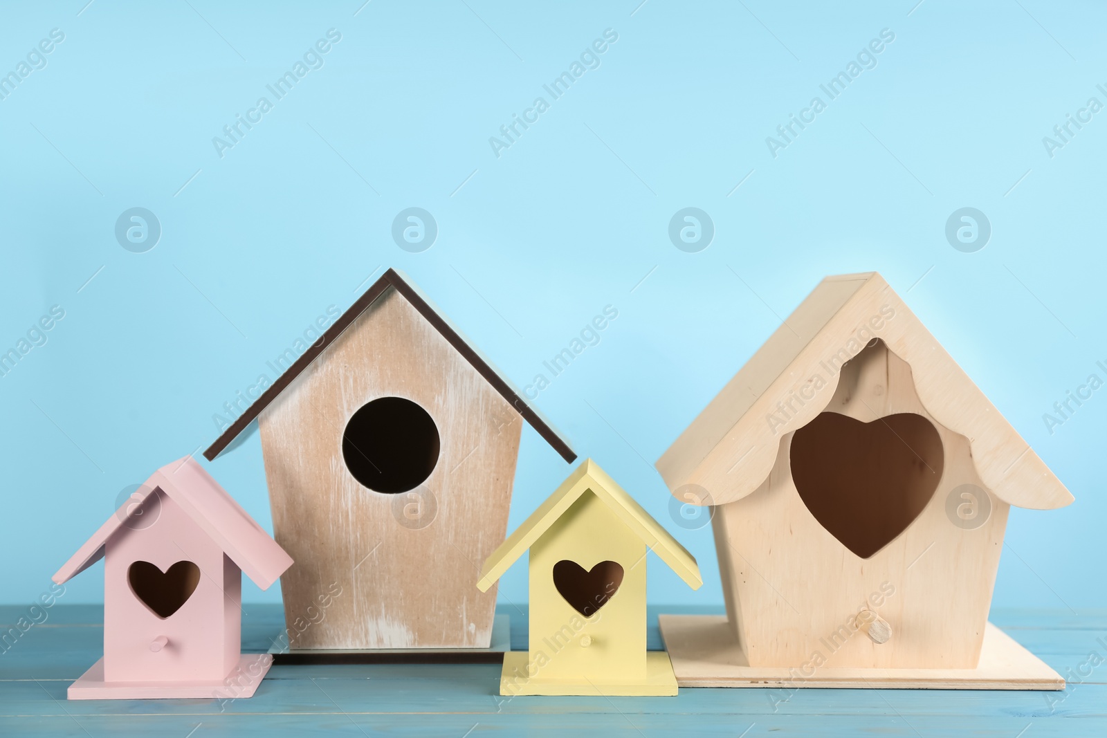 Photo of Beautiful bird houses on wooden table against light blue background